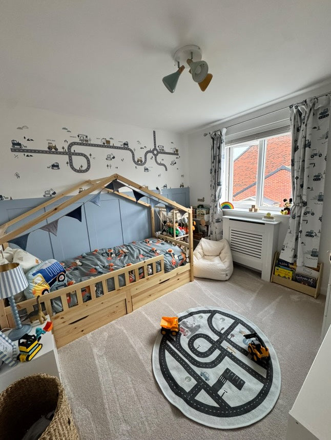 Smiling child enjoying a cozy nursery space adorned with peel-and-stick truck, tractor, and digger wall decals from Nursery Stickers